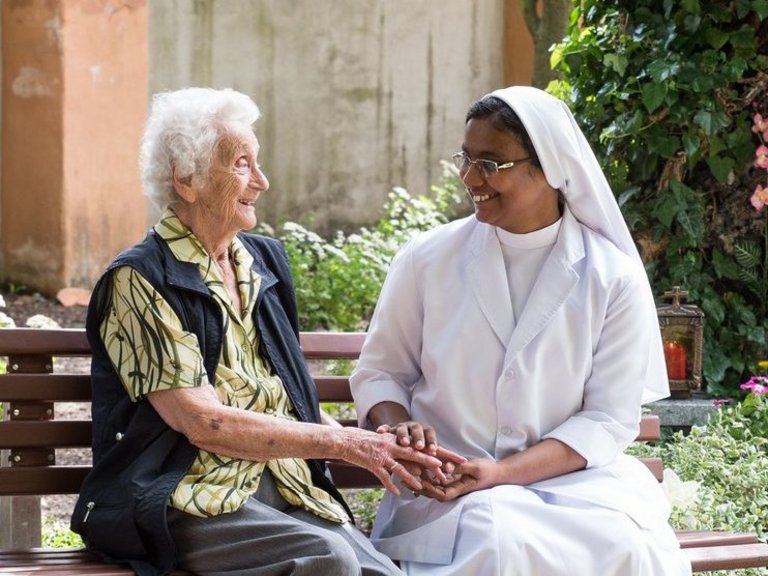 im Garten auf einer Bank: eine Ordensschwester hält die Hand einer Bewohnerin